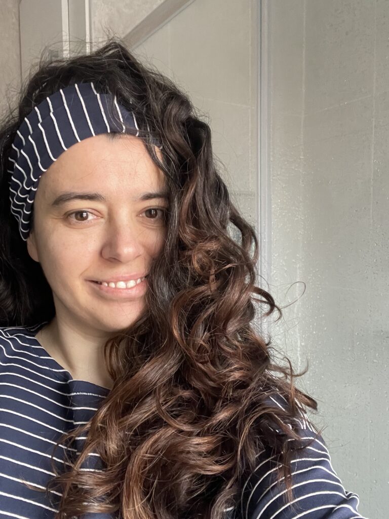 Image of a women with long darkbrown curly hair in a navy and white striped top and matching headband