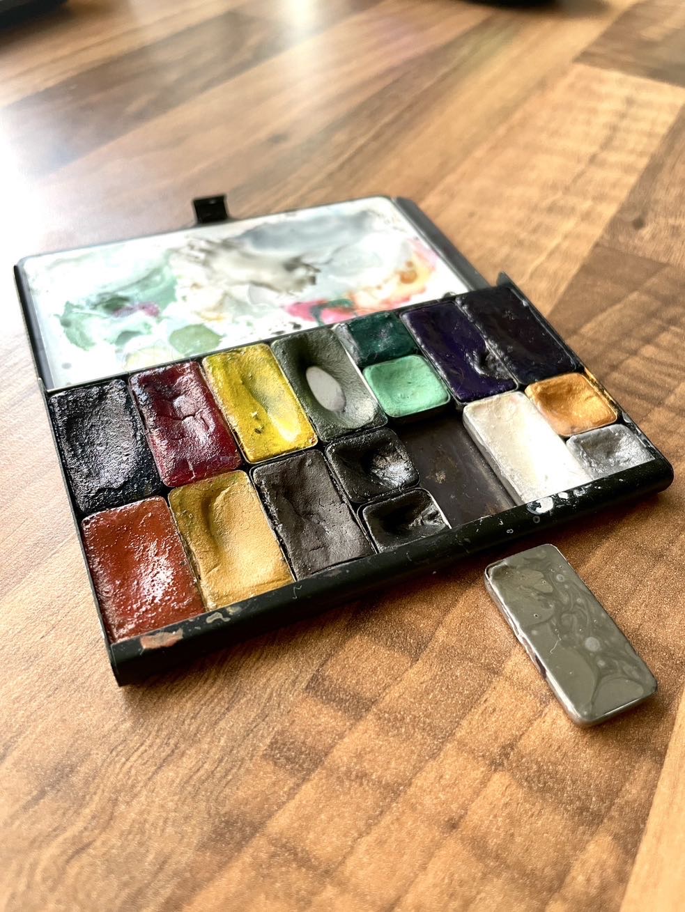 Photograph showing a small ArtToolKit palette with a single pan of pan set out separate from it which is grey in colour.