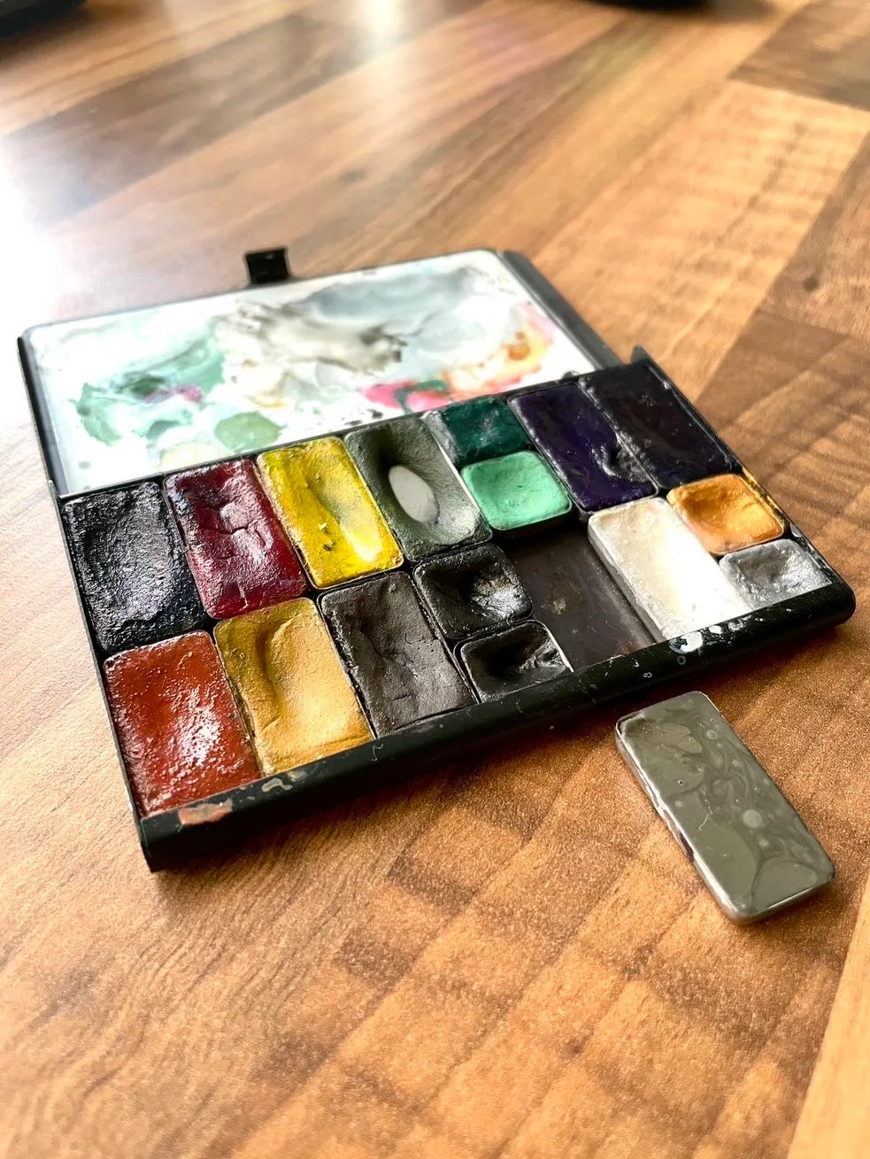 Photograph showing a small ArtToolKit palette with a single pan of pan set out separate from it which is grey in colour.
