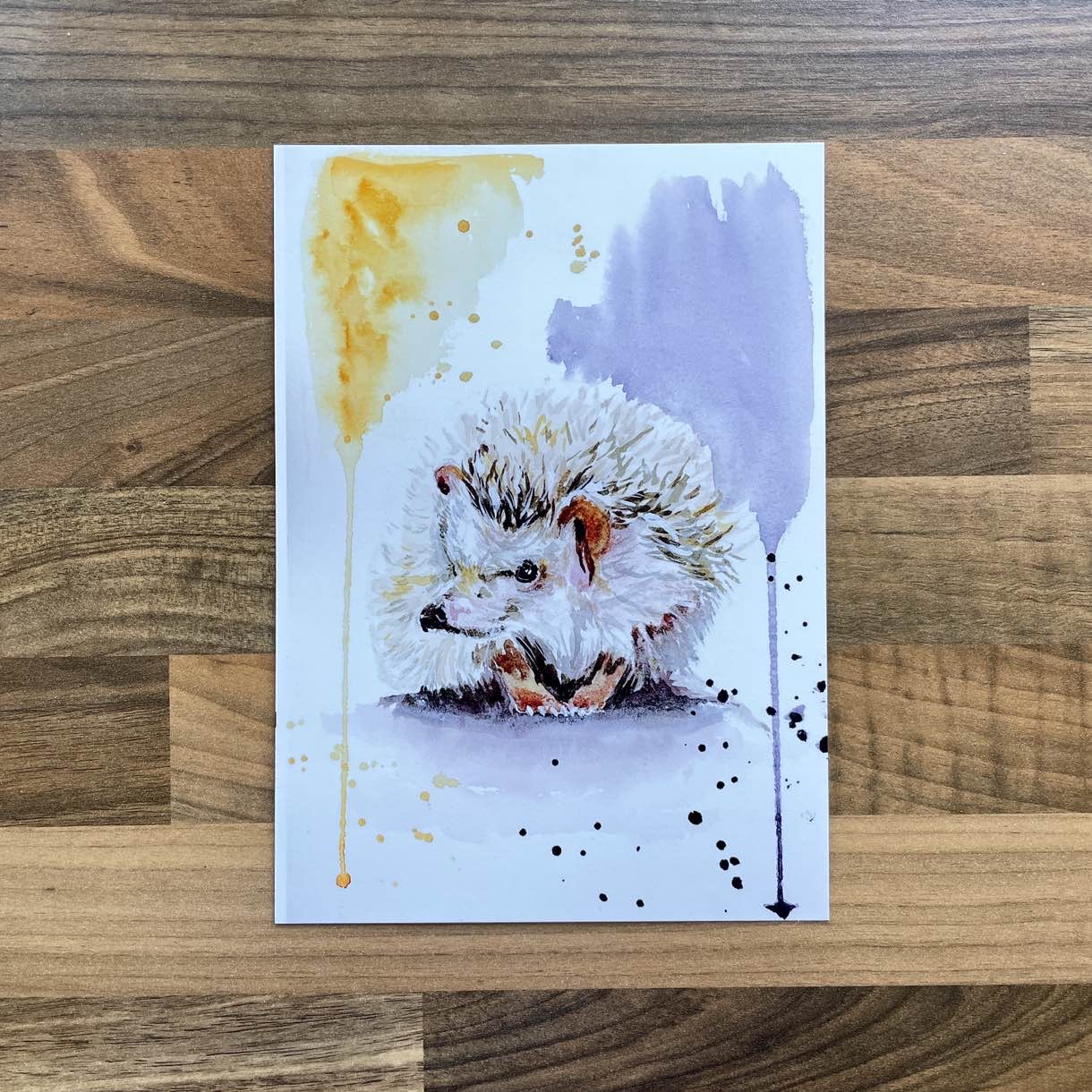 Watercolour painting of a hedgehog with playful yellow and purple paint splashes
