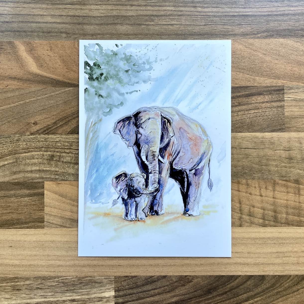 Watercolour painting of a mother elephant with a small baby holding their trunk