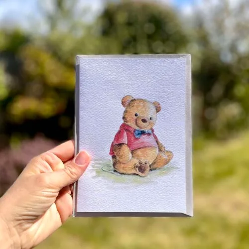 Watercolour teddy bear weaing a red top and blue bowtie on an A5 greetings card